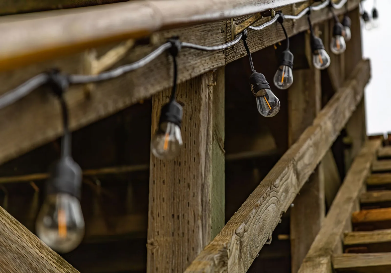 Deck lighting ideas with warm post cap lights and recessed stair lights on a wooden deck at dusk
